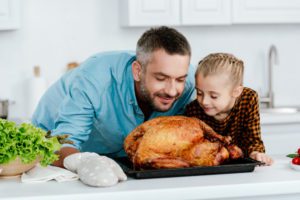 happy father and daughter sniffing freshly baked thanksgiving turkey