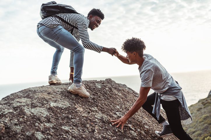 Young man helping his friend to climb the rock